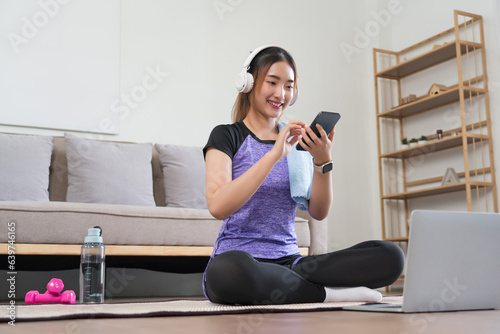 Young asian woman use smartphone to listening music after watching fitness video to doing exercise