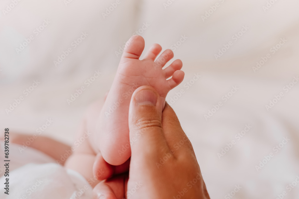 Parent holding in hand feet of newborn baby lying on cozy white bed. Unknown father making foot massage for newborn baby. Dad and little child. Happy Family concept. Copy space for promotion content Parent holding in hand feet of newborn baby lying on cozy white bed. Unknown father making foot massage for newborn baby. Dad and little child. Happy Family concept. Copy space for promotion content