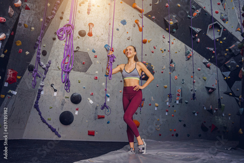 A strong female climber against an artificial wall with colorful grips and ropes.