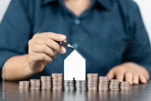 Saving money for house and real estate. Woman hand pointing on stack coins and house model on table.