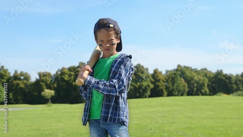 Portrait of serious lovely school age African American boy baseball hitter with baseball bat wearing eye black, ready to hit a shot and waiting for pitch while enjoying playing game on green field.