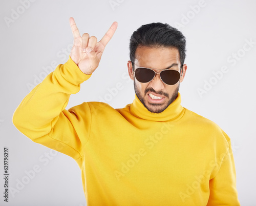 Man, sunglasses and horns sign in studio portrait, rock icon or hand gesture with clothes by white background. Young guy, model and devil fingers for attitude, fashion or crazy with emoji for culture