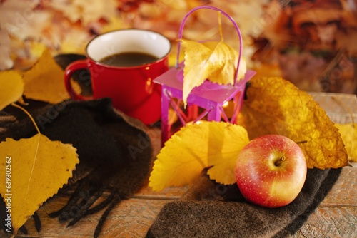 Autumn still life with a cup of coffee, an apple, a lantern and a cashmere scarf against the background of fallen autumn leaves