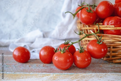 Ripe red cherry tomatoes in a wicker basket on a wooden background.