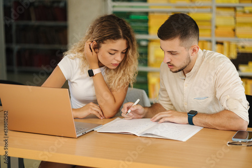 Boy help his girlfriend preparing for exam in public library. Education concept © Aleksandr