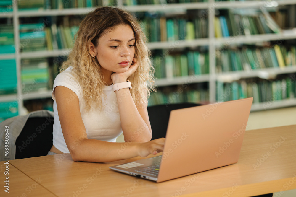 Pretty girl student study in library using laptop. Back view of books. Education concept Pretty girl student study in library using laptop. Back view of books. Education concept