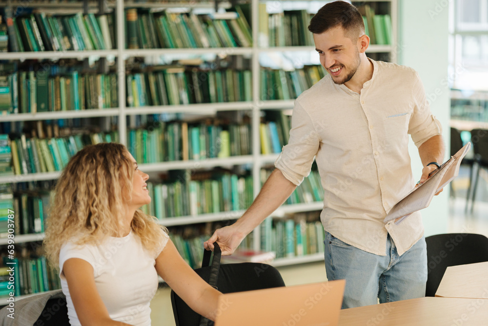 Girl sitting in library and waiting for classmate. Student come and kiss female Girl sitting in library and waiting for classmate. Student come and kiss female