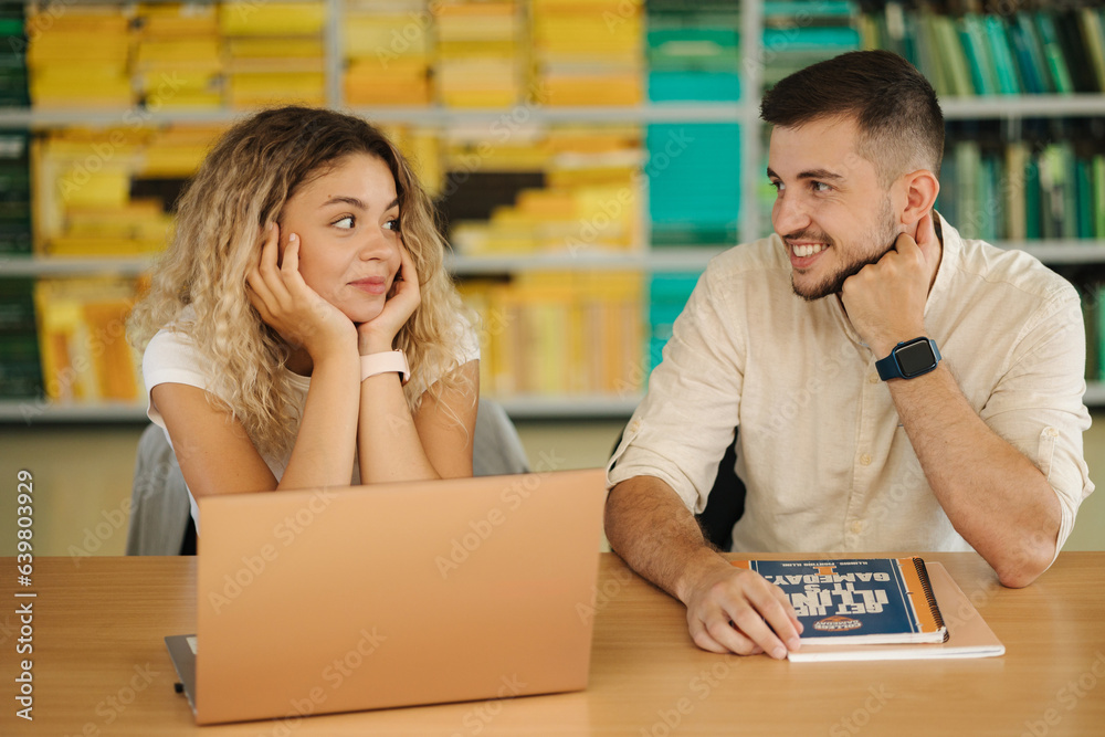 Pretty girl student look into laptop and don't know how to complete the task. Boy help female classmate in library Pretty girl student look into laptop and don't know how to complete the task. Boy help female classmate in library