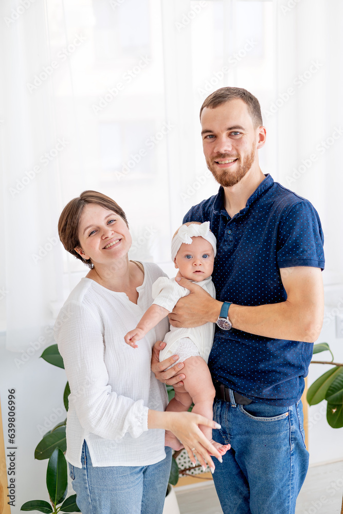 happy family mom, dad and little baby daughter hug and kiss, a young family at home with a newborn baby