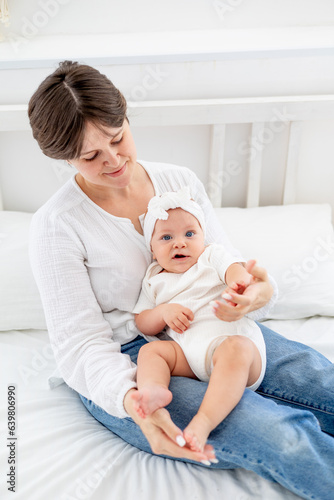 mom gently hugs her baby daughter kissing and admiring them, happy family, mom with baby on the bed, maternal love and care, mom on maternity leave playing with the baby