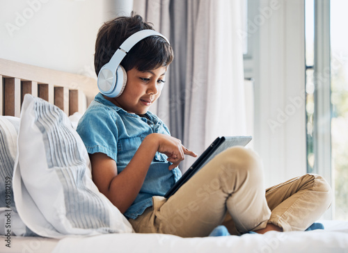 Boy, kid and headphones with tablet on bed for online games, watching movies or play educational app. Happy child, digital technology or listening to multimedia, music or streaming cartoon in bedroom