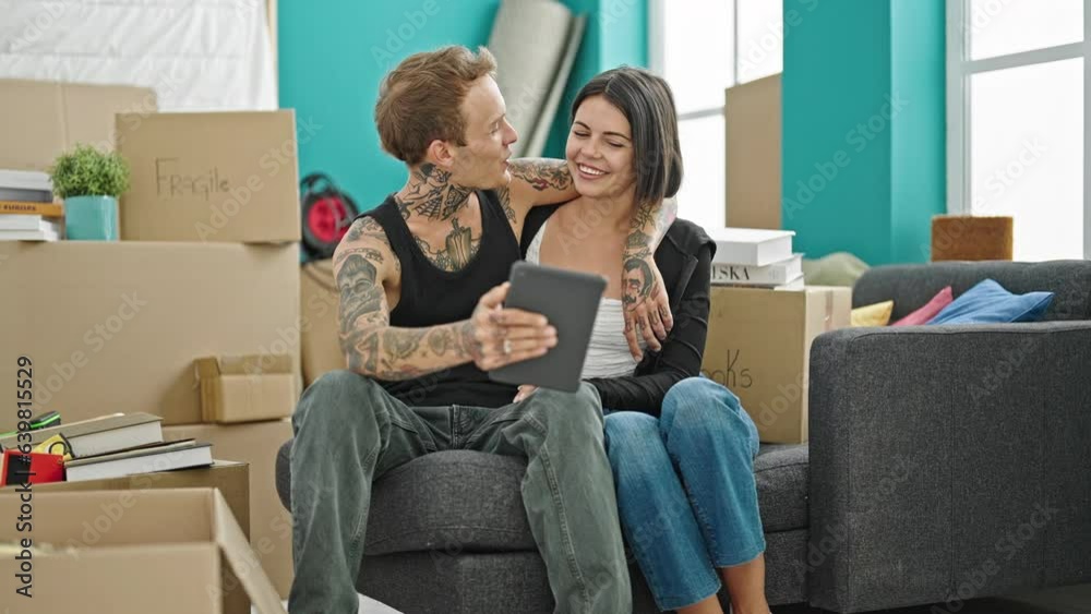 Beautiful couple hugging each other using touchpad smiling at new home Beautiful couple hugging each other using touchpad smiling at new home