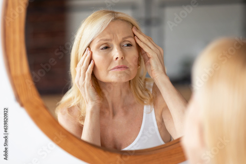 Εκτύπωση καμβά Upset middle aged woman looking at mirror and touching wrinkles on her face, lad