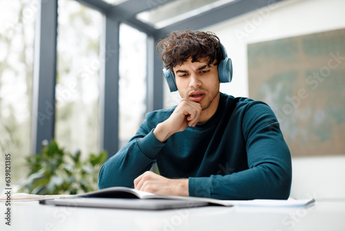 European guy listening online lecture and doing his home assigment looking attentively in copybook, sitting in audience photo