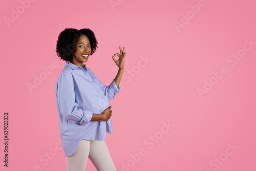 Happy young black pregnant woman in casual touching big belly, show ok sign with hand, enjoy motherhood