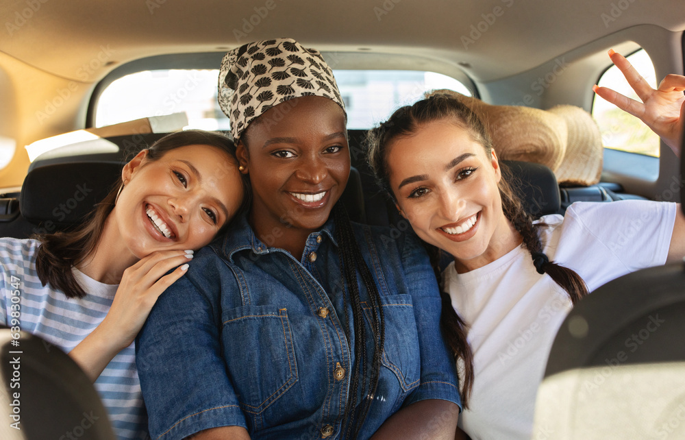 Cheerful multiracial girlfriends riding car together, smiling at camera