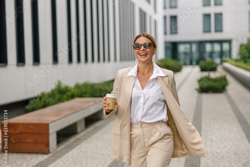 Happy woman entrepreneur with coffee walking on modern building background during break time