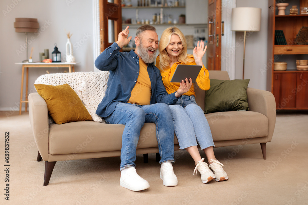 Senior Couple Making Video Call Via Tablet Waving Hand Indoors