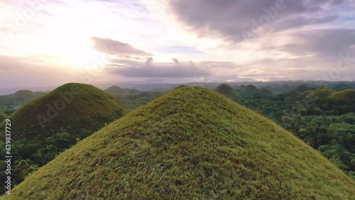 Chocolate Hills at sunset in Bohol Island, Philippines. Aerial drone cinematic shot. Orbit backward travelling close to hills. Famous tourist landmark. Vibrant dusk colors and dramatic cloudy sunset.