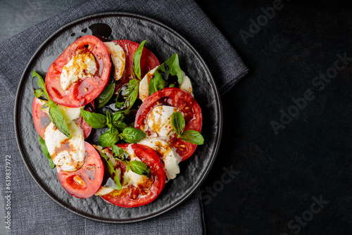 Caprese salad made of sliced fresh tomatoes, mozzarella cheese and basil served on black plate. Top view. Copy space