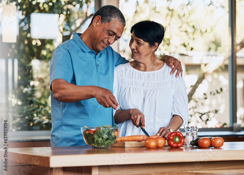 Happy couple, love and hug while cooking food, cutting carrot and prepare vegetables for salad at home. Mature man, smile and embrace woman in kitchen to make healthy lunch, meal and diet for dinner