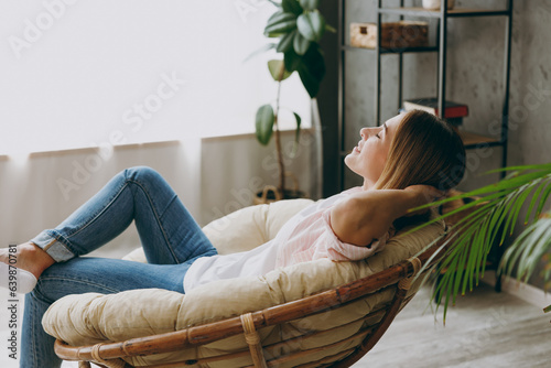 Photography Side profile back view calm blonde young woman wearing casual clothes sit in armchair look camera stay at home hotel flat rest relax spend free spare time in living room indoor