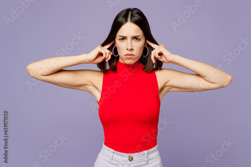 Young sad woman she wearing red tank shirt casual clothes closed eyes covering ears with hands fingers do not want to listen scream isolated on plain pastel light purple background. Lifestyle concept.