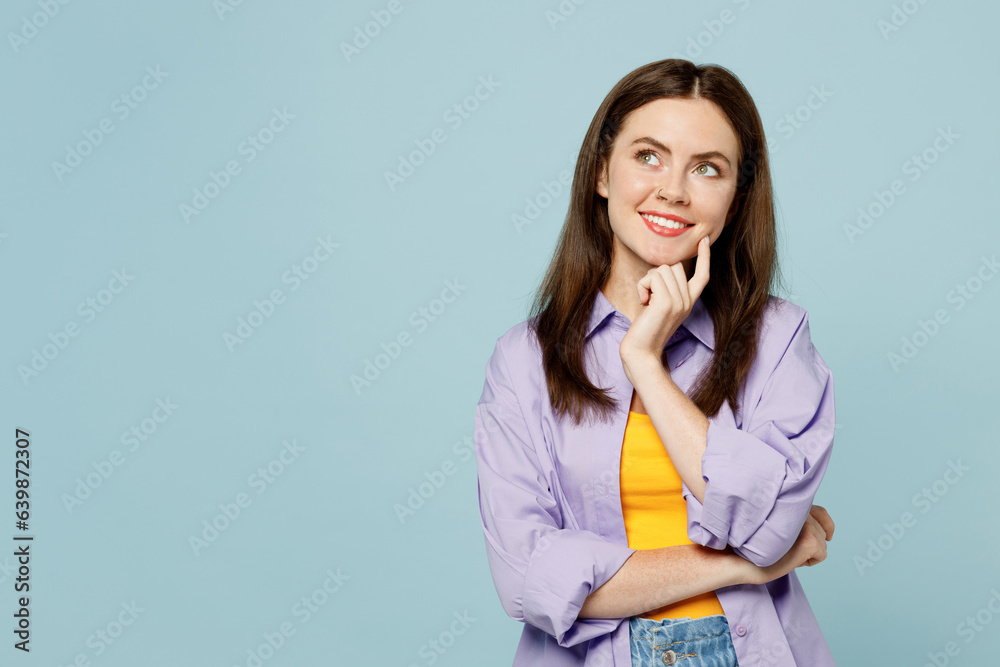 Young happy woman she wear purple shirt yellow t-shirt casual clothes put hand prop up on chin, lost in thought and conjectures isolated on plain pastel light blue background studio Lifestyle concept Young happy woman she wear purple shirt yellow t-shirt casual clothes put hand prop up on chin, lost in thought and conjectures isolated on plain pastel light blue background studio Lifestyle concept