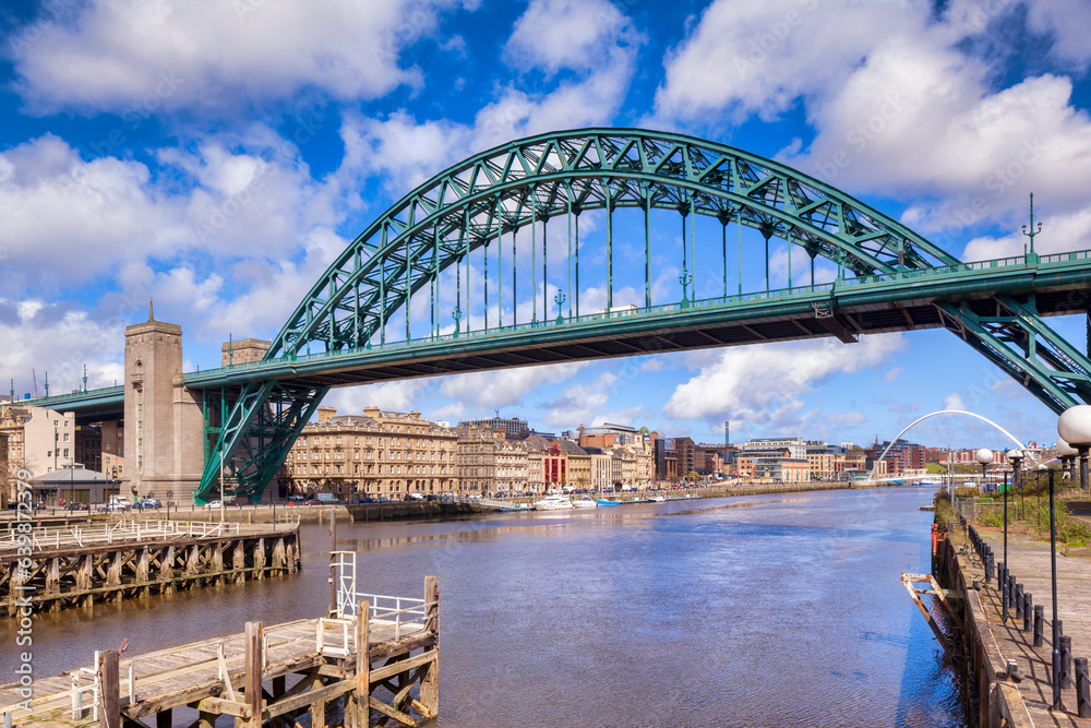 Newcastle upon Tyne, UK - the Tyne Bridge and the River Tyne, in the North East of England, UK, on a bright spring day, with historic waterside buildings on the banks and blue sky with  white clouds.