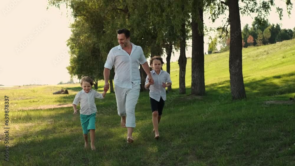 Father and two sons run through the grass holding hands Father and two sons run through the grass holding hands