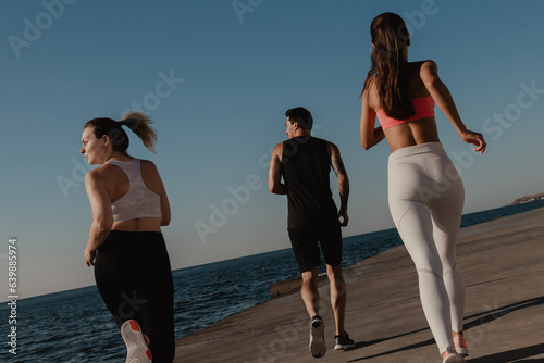 Fotografija Rear view of three young people in sportswear enjoying morning jog seaside toget
