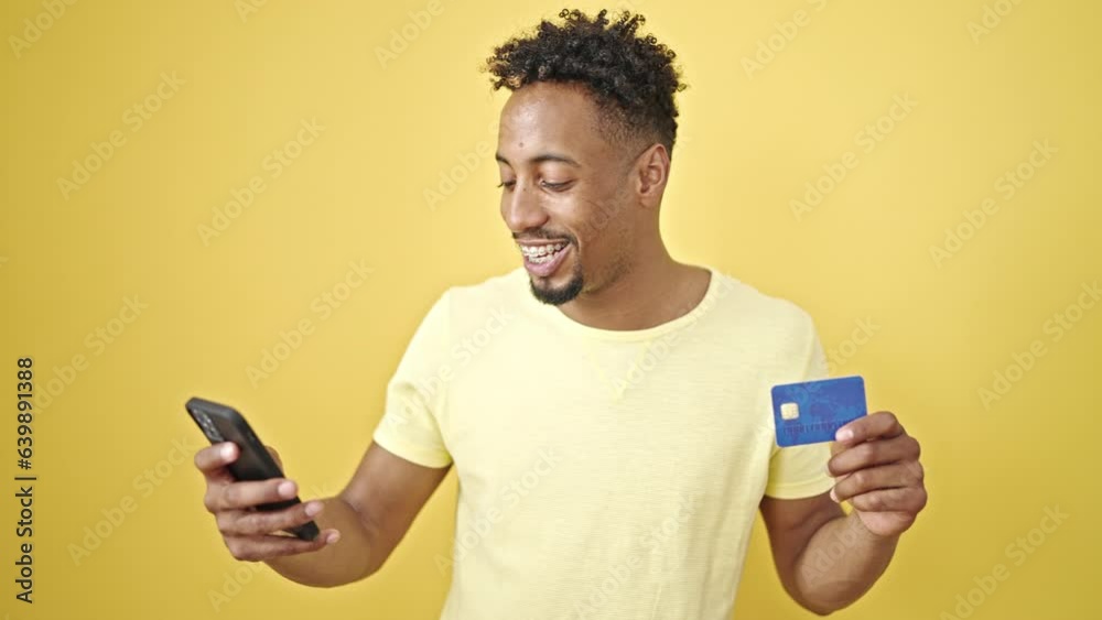 African american man shopping with smartphone and credit card celebrating over isolated yellow background