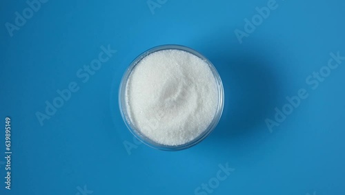 Sodium citrate powder on glass bowl on blue background, top view. Food additive E331, preservative and flavoring. Its properties are similar to Calcium Citrate (E333). photo