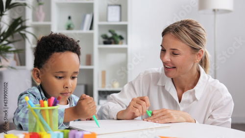 Adorable little african american boy with curly hair having fun at pediatric specialist appointment, happy child drawing with female therapist, exercises for children with autism.