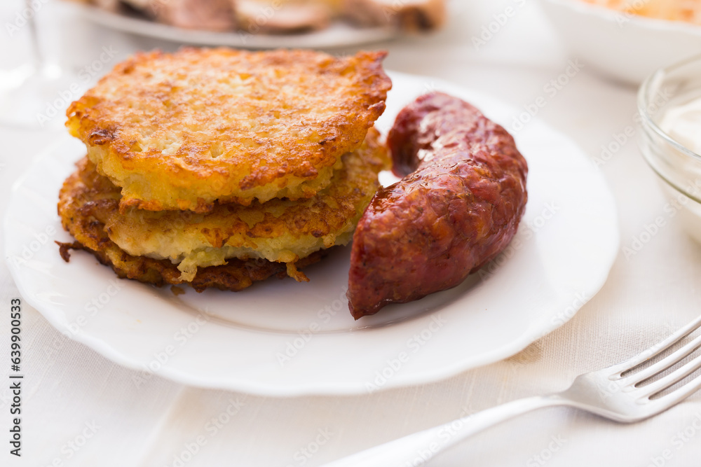 Potato pancakes with fried sausage on white plate Potato pancakes with fried sausage on white plate