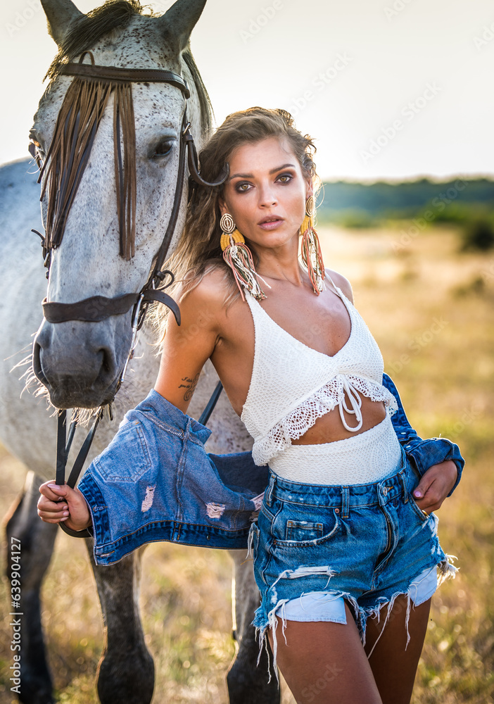 Beautiful blonde woman with curly hair with white hat and horse. Portrait of a girl with denim and her horse. Beautiful girl interacting and having fun with a horse at the ranch