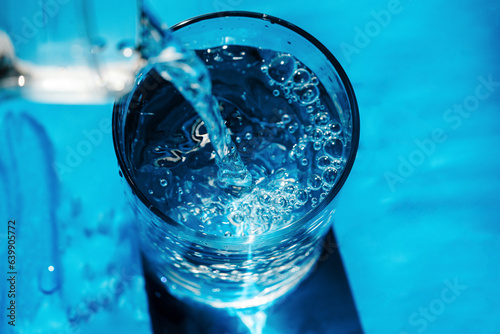 water jet pours from bottle into glass top view on blue background
