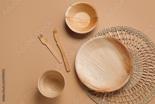 Wooden plate, bowls, wicker mat and cutlery on beige background