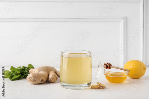 Fotografia Glass cup of ginger tea and bowl with honey on white background