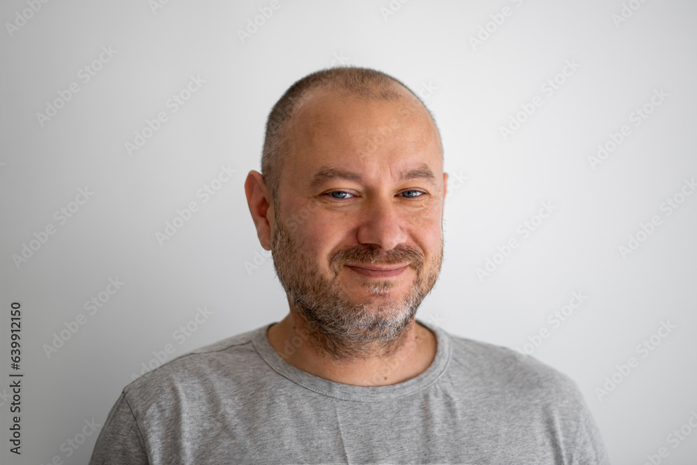 A man of ordinary appearance unshaven smiles and looks at the camera on a gray background. A man in his forties. A man of ordinary appearance unshaven smiles and looks at the camera on a gray background. A man in his forties.
