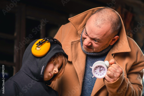 A man shakes an alarm clock in front of a young tired boy. The process of misperception concept. photo