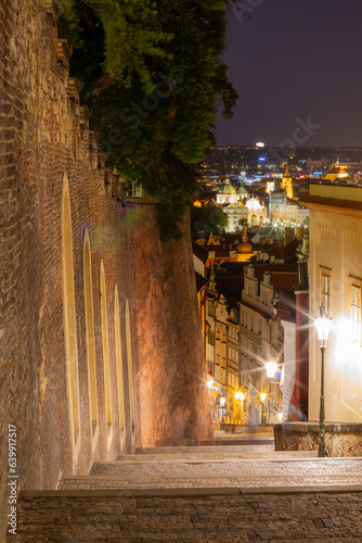 Stunning nighttime view of illuminated downtown Prague, taken from a quaint cobblestone alleyway on the hilltop next to the walls of Prague Castle