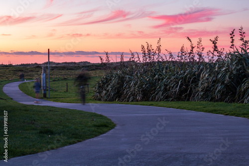 People enjoying the setting sun over the coastal dunes while going for evening walks or bike rides along the Coastal Walkway outside of New Plymouth, New Zealand