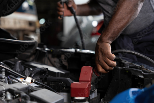 close up mechanic worker hands holding battery cable for jumping battery of a car in automobile repair shop