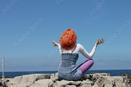 Red head woman meditating on a rock on the day light