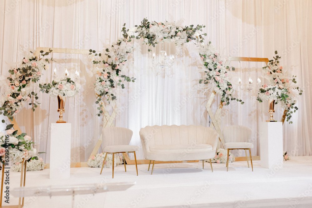 Beautiful decor for the wedding ceremony in the form of a sofa and white flowers on the wedding arch. White furniture in the form of a sofa and armchairs for the bride and groom