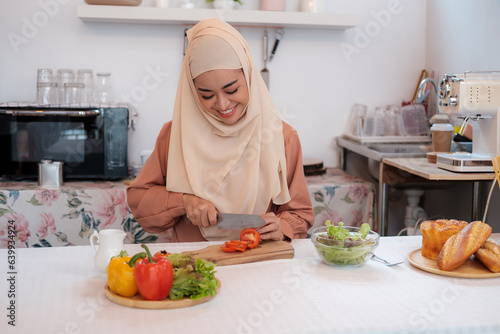 Mature muslim islamic woman in hijab mixing preparing cooking vegetable salad in the kitchen. Vegan vegetarian food concept.