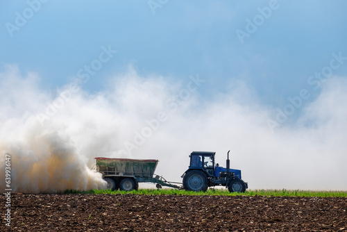 Tractor spreading potash fertilizer on green wheat field.  Farmer spreading potash fertilizers. Agriculture vehicle spraying field.