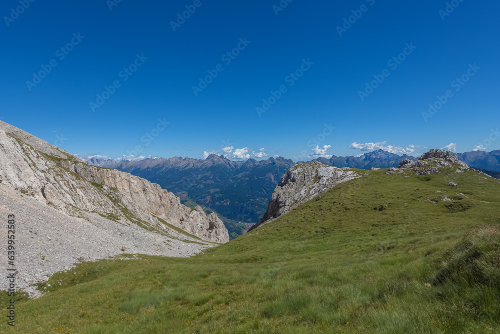 Meadows and rocky ridges in the southern side of the Latemar Massif. Lagorai mountain range in the background. UNESCO world heritage site, Trentino-Alto Adige, Italy, Europe