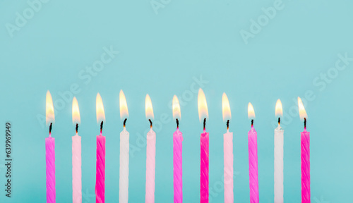 11 pink and white color birthday candles burning in a row isolated on blue. Happy Birthday card design concept.  Bottom lower border edge a lot of copy space. 